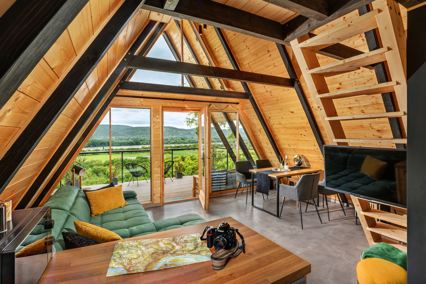 324-duna-zen-ga Verőcei faszerkezetű nyaraló fő belső tere, előtérben térképpel, bútorzattal, Visegrási-hegységi panorámával, fényfestéssel fotózva